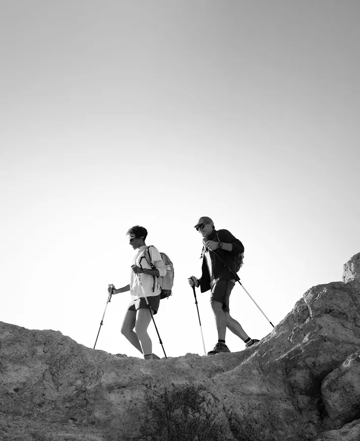 Фото двох туристів із трекінговими палицями, які йдуть скелястим гірським маршрутом. На зап'ястях мандрівників — смарт-годинники Apple Watch Ultra 3, що підкреслює призначення гаджета для складних походів, навігації в горах та тривалих експедицій