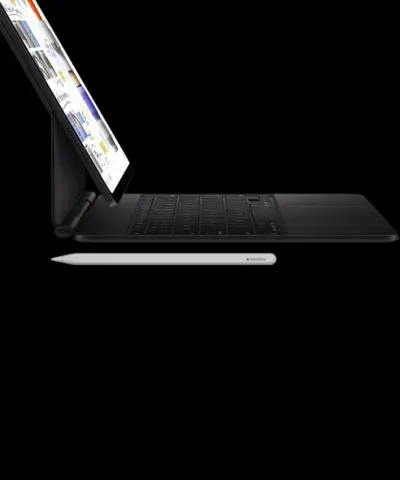 Планшет Apple iPad Pro M5, підключений до чорної клавіатури Magic Keyboard з трекпадом, у режимі ноутбука. На передньому плані розташований білий стилус Apple Pencil Pro. Демонстрація повноцінного робочого сетапу та преміальної екосистеми аксесуарів Apple