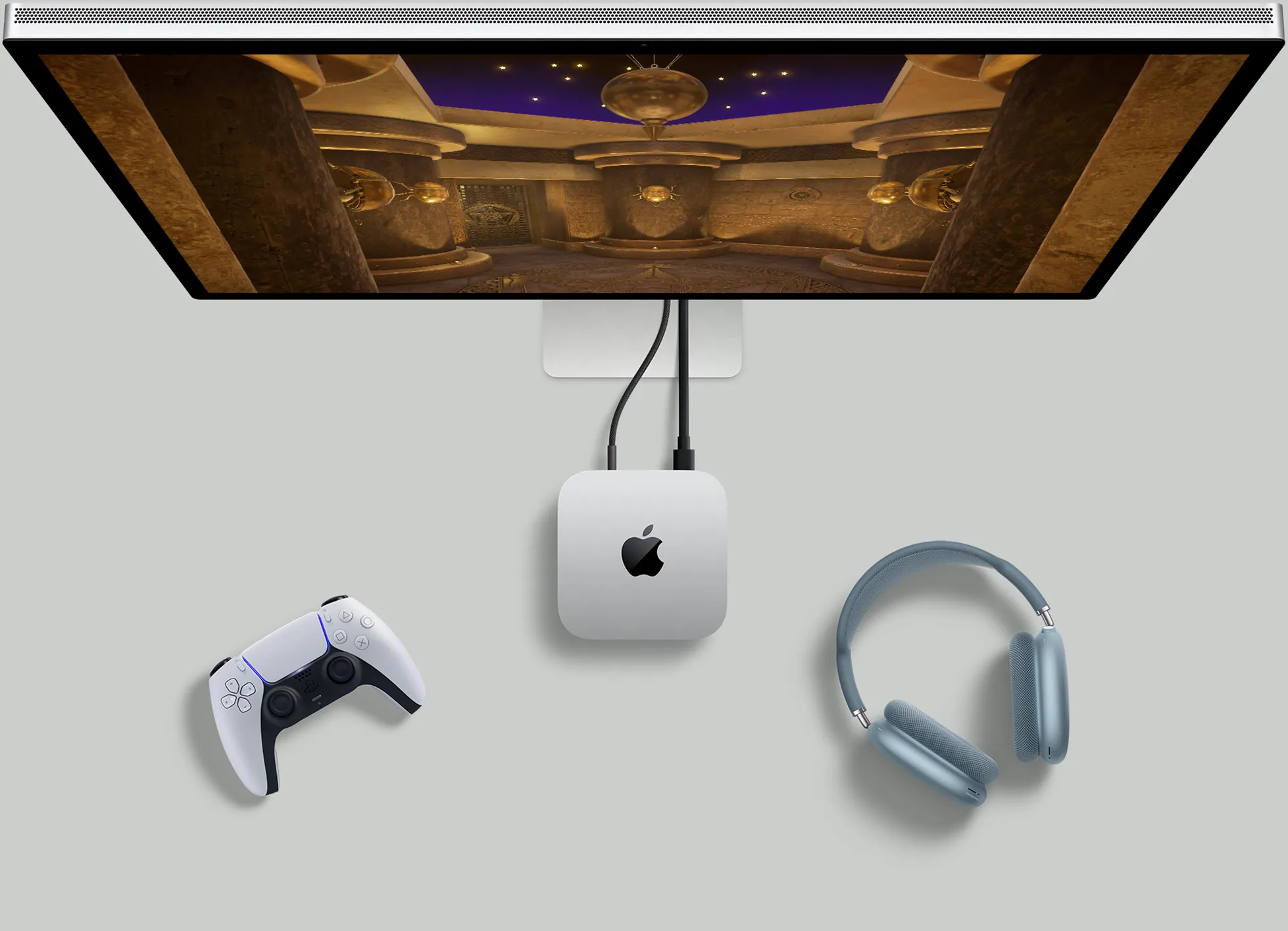 Вид зверху на сріблястий Mac mini, який розміщено на столі поряд із монітором з активним екраном, бездротовими клавіатурами, бездротовими мишами, ігровим контролером і навушниками AirPods Max